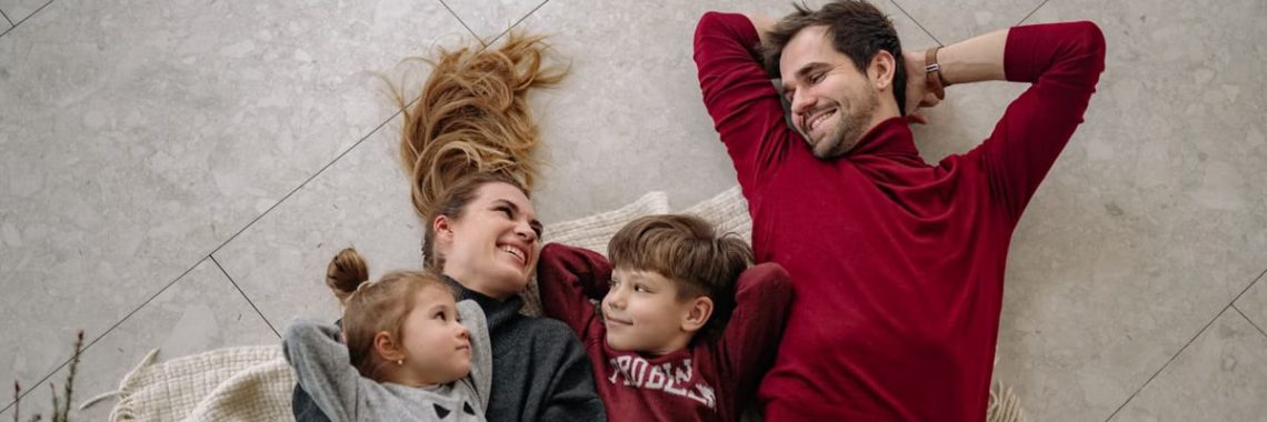 Smiling family of four lying on a blanket, sharing happiness and love indoors.
