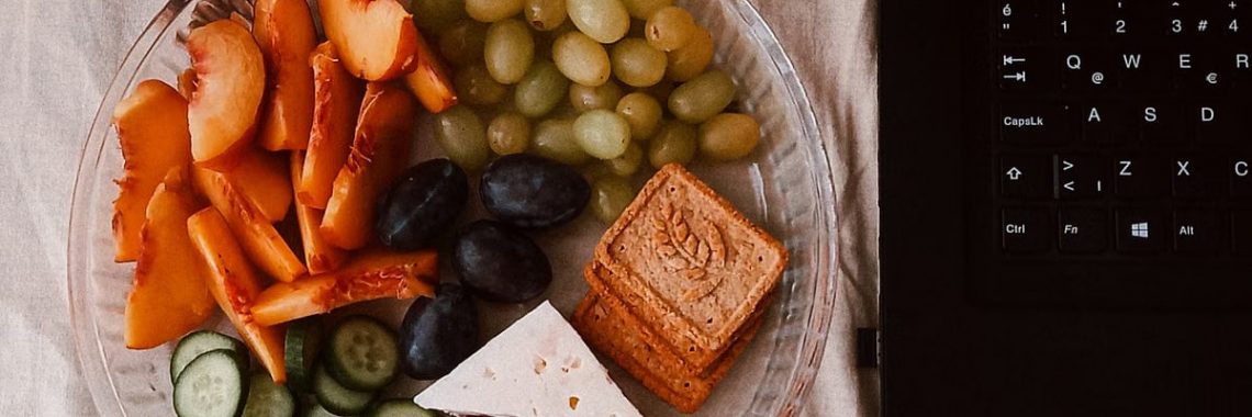A delightful snack plate with fruits, cheese, and a laptop for a healthy lifestyle.